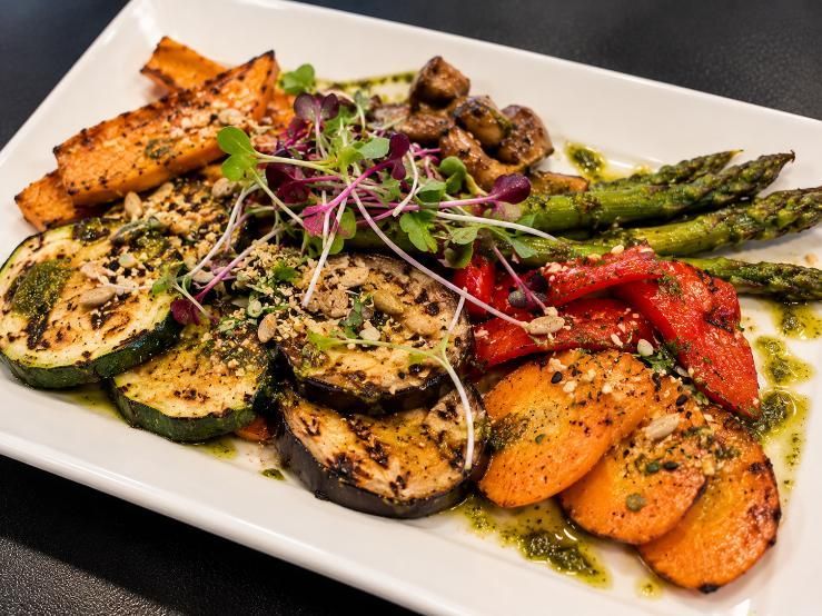 Verduras a la parrilla y espárragos en un plato blanco, adornados con hierbas y semillas