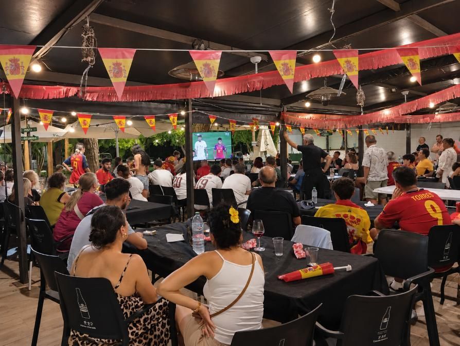 Personas sentadas bajo una carpa viendo a una banda tocar en directo sobre un escenario muy iluminado durante un evento