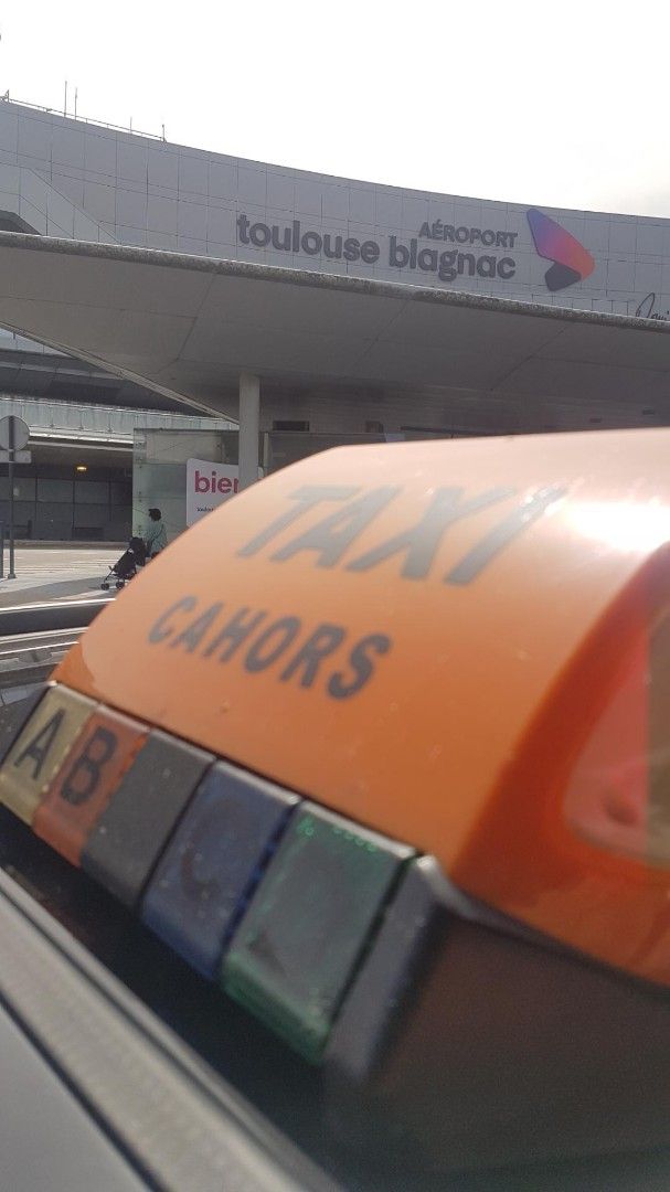 Enseigne de taxi orange sur le toit, avec compteur lumineux, garée près de l’entrée d’un bâtiment