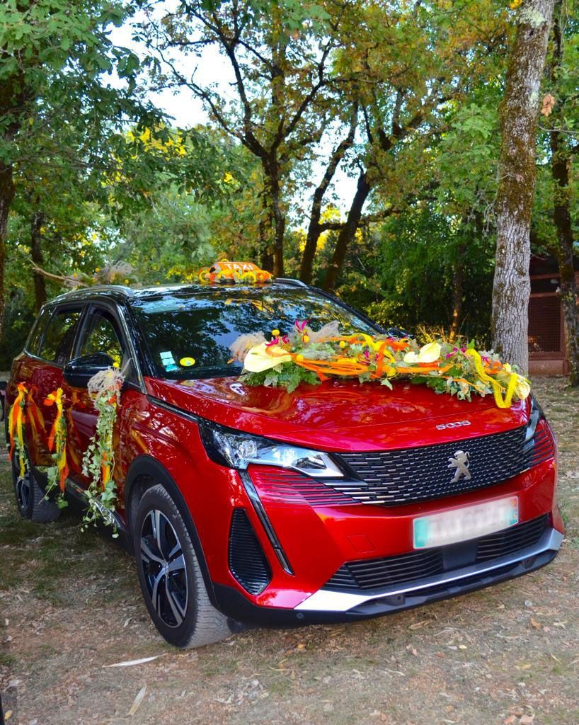 SUV rouge décoré de fleurs et de rubans, garé sur un chemin boisé en plein air.