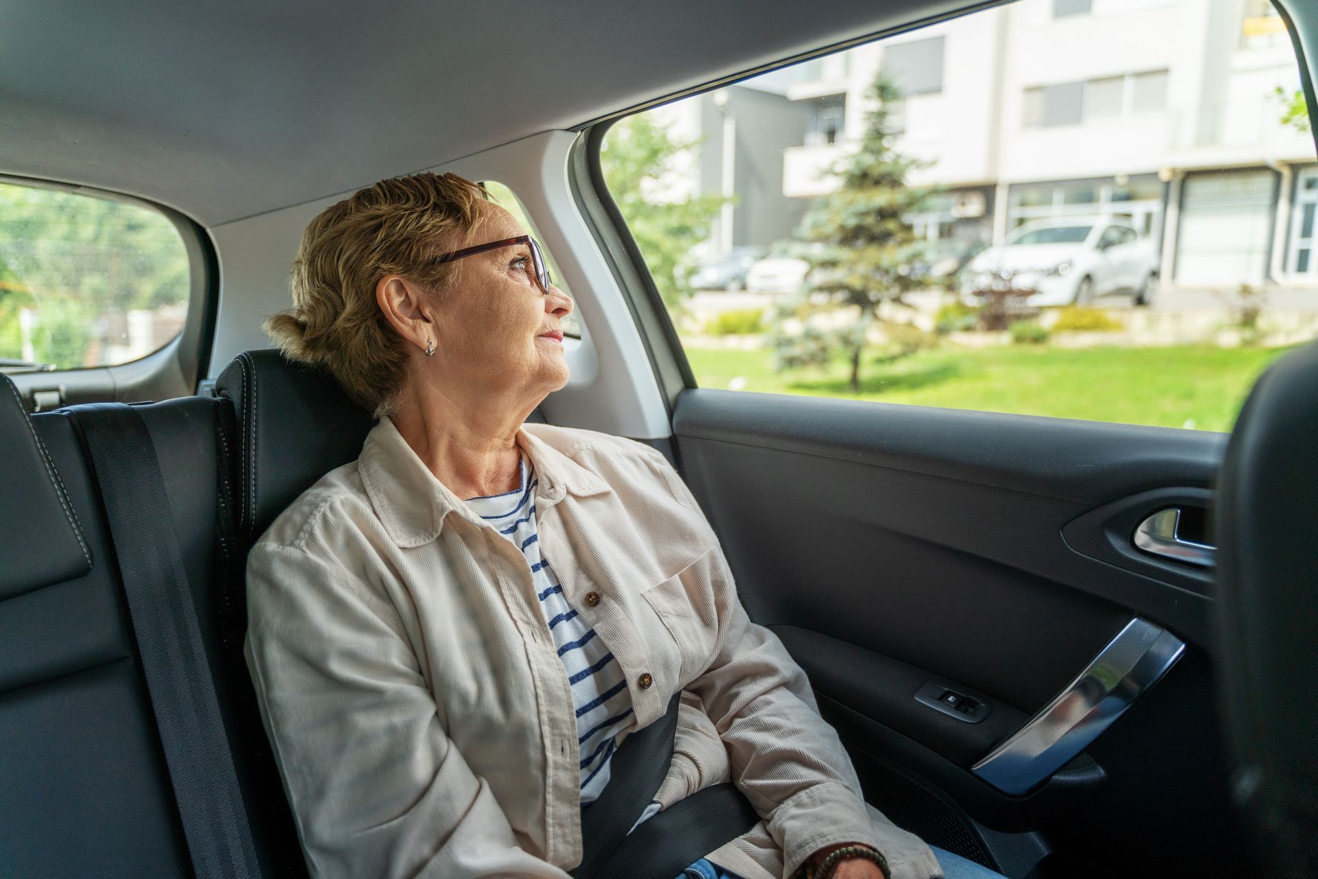 Une femme est assise dans une voiture et regarde par la fenêtre les bâtiments à l’extérieur.