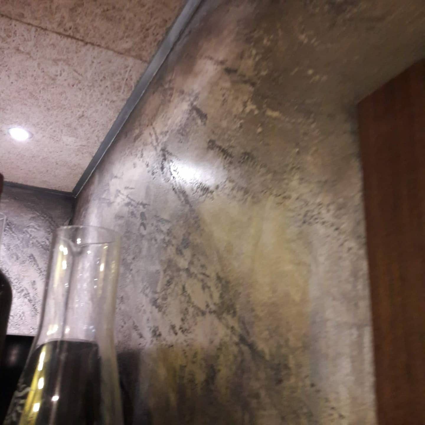 Una botella oscura en primer plano, frente a una pared y un techo marmoleados y reflectantes, en un interior con poca luz