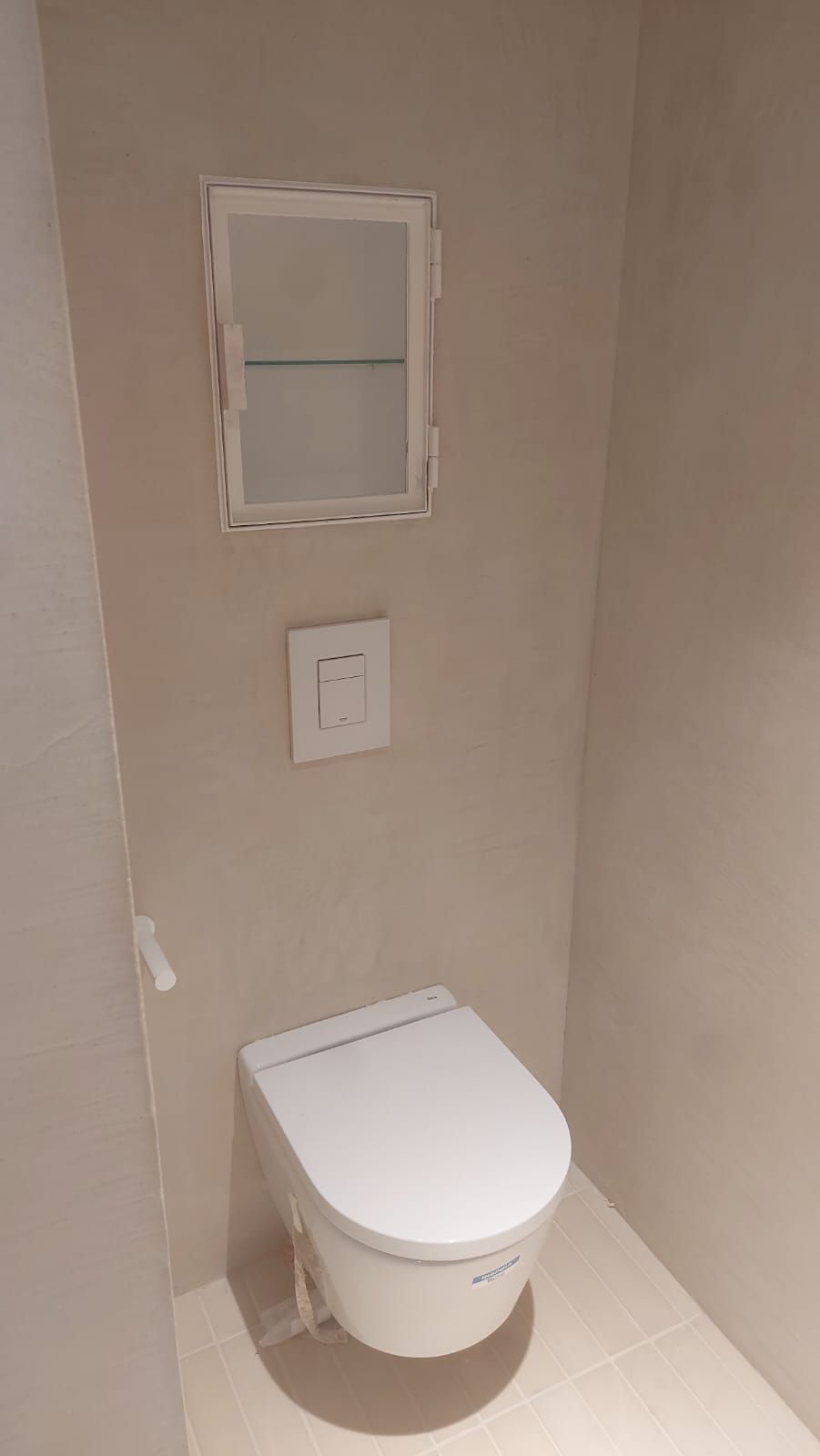 Baño pequeño de color beige, con un inodoro suspendido y una pequeña ventana esmerilada encima.