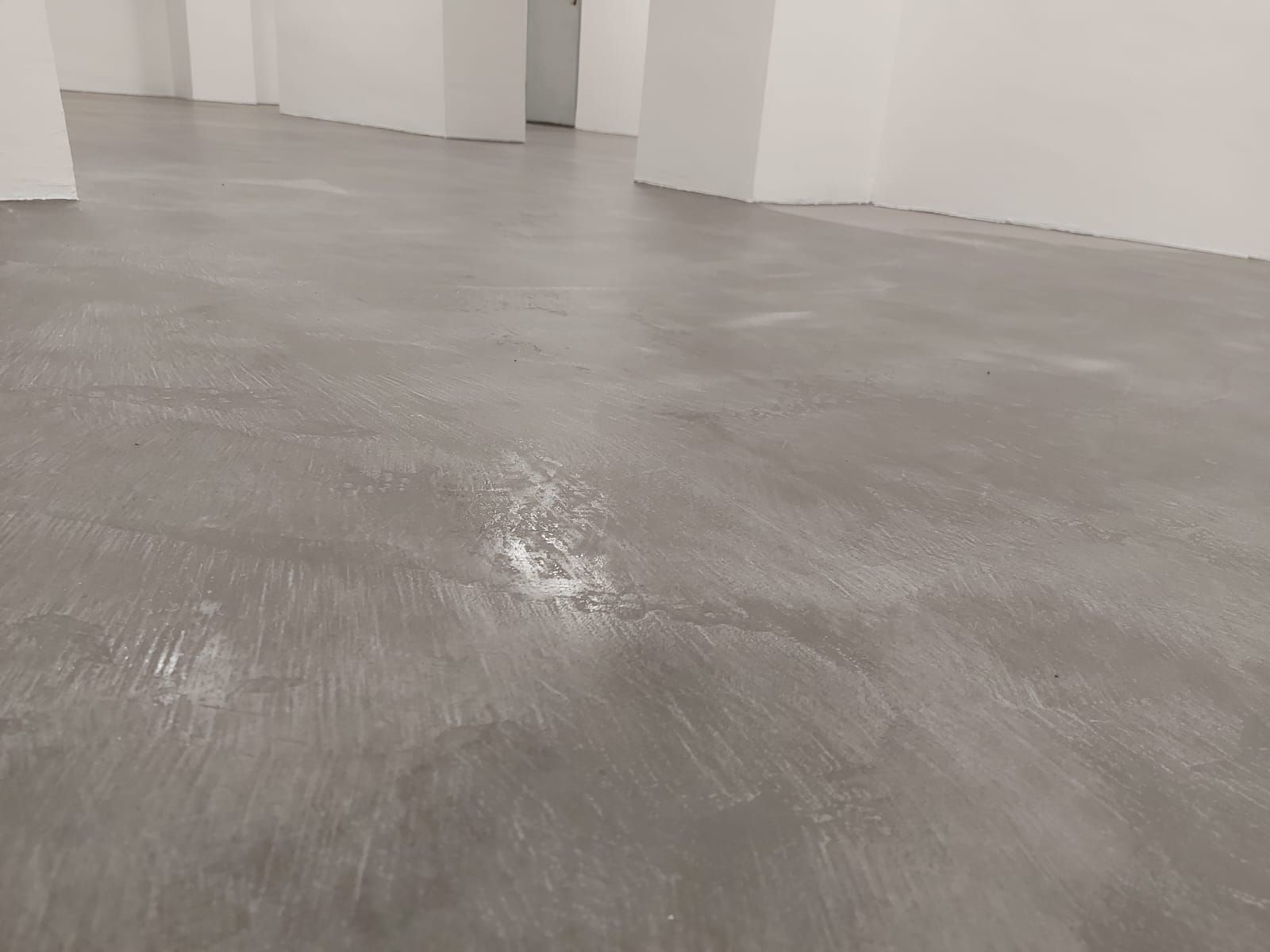 Suelo de hormigón gris vacío en una habitación blanca sin muebles, con una pequeña zona mojada en el centro