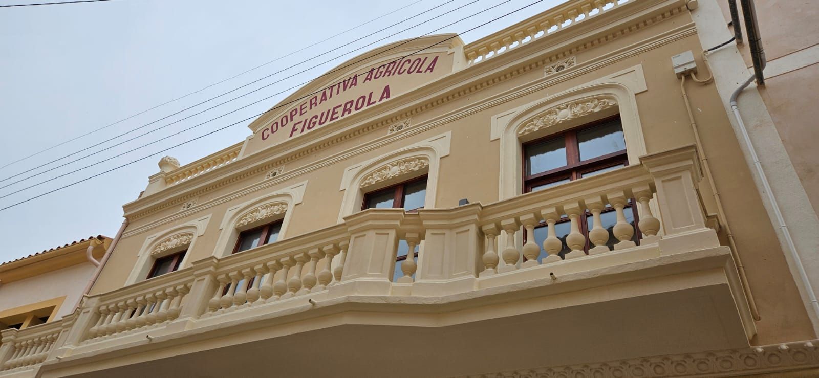 Vista en contrapicado de un edificio histórico de color beige, con un balcón ornamentado y ventanas arqueada