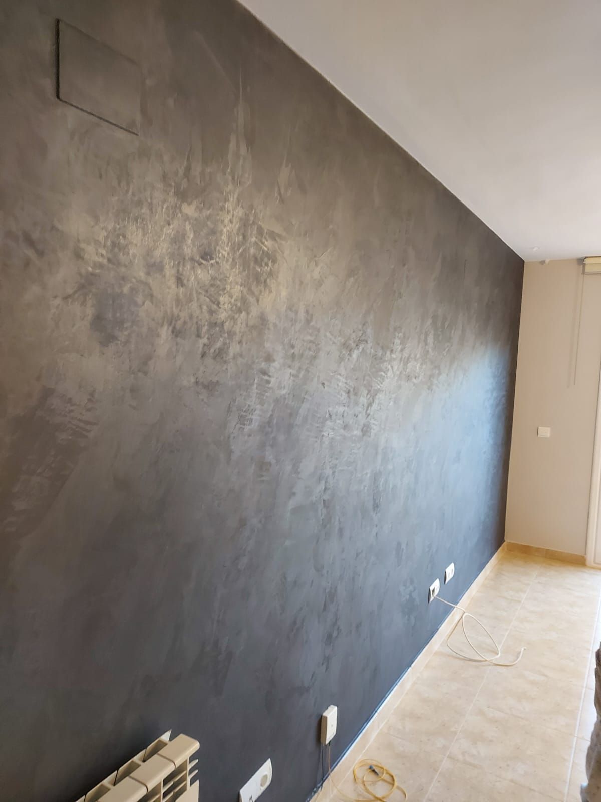 Habitación vacía con una pared de acento gris oscuro y textura, suelo de baldosas claras y ventanas