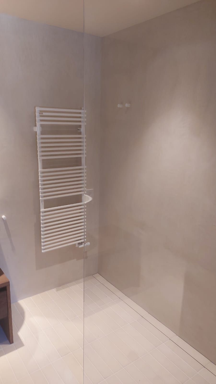 Ducha vacía de color beige con radiador toallero blanco montado en la pared y suelo de baldosas