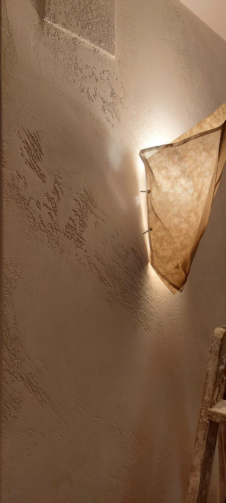 Aplique de pared cálido con pantalla beige que proyecta luz sobre una pared color crema con textura