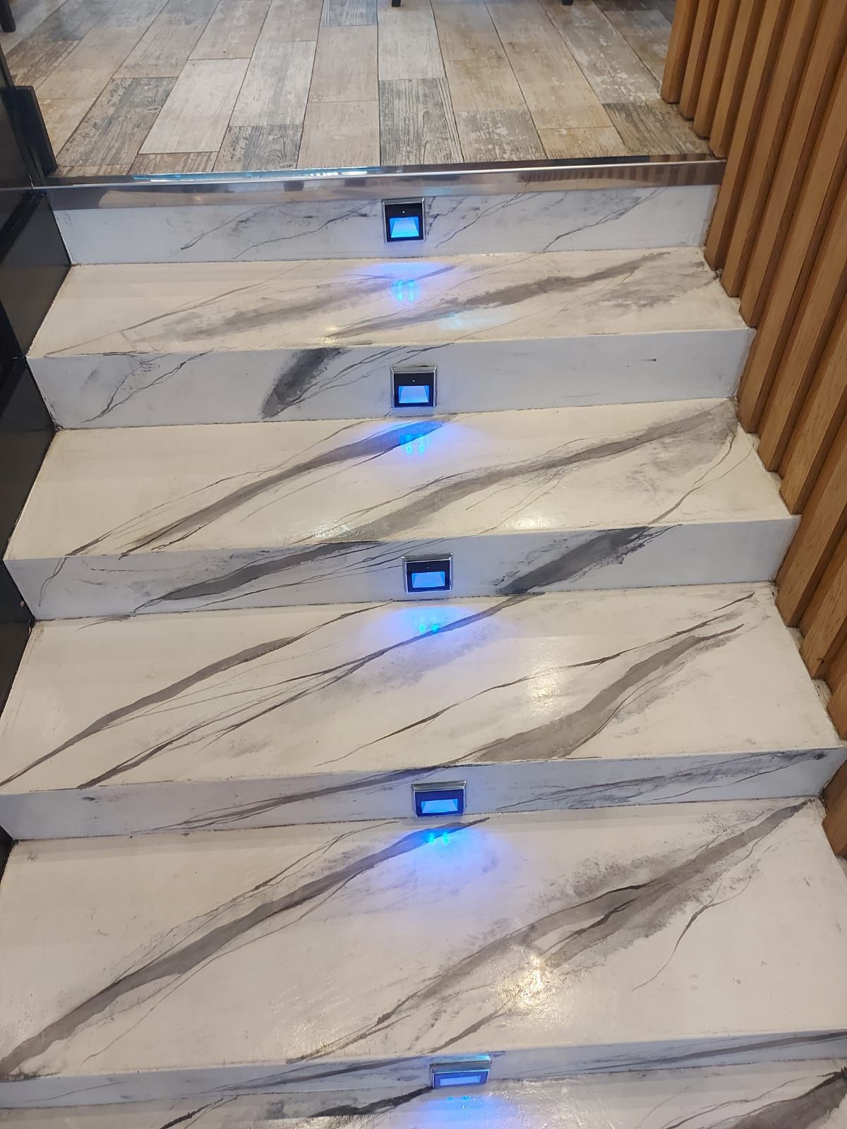 Escalera de mármol con vetas grises y luces LED azules en los escalones que suben hacia arriba