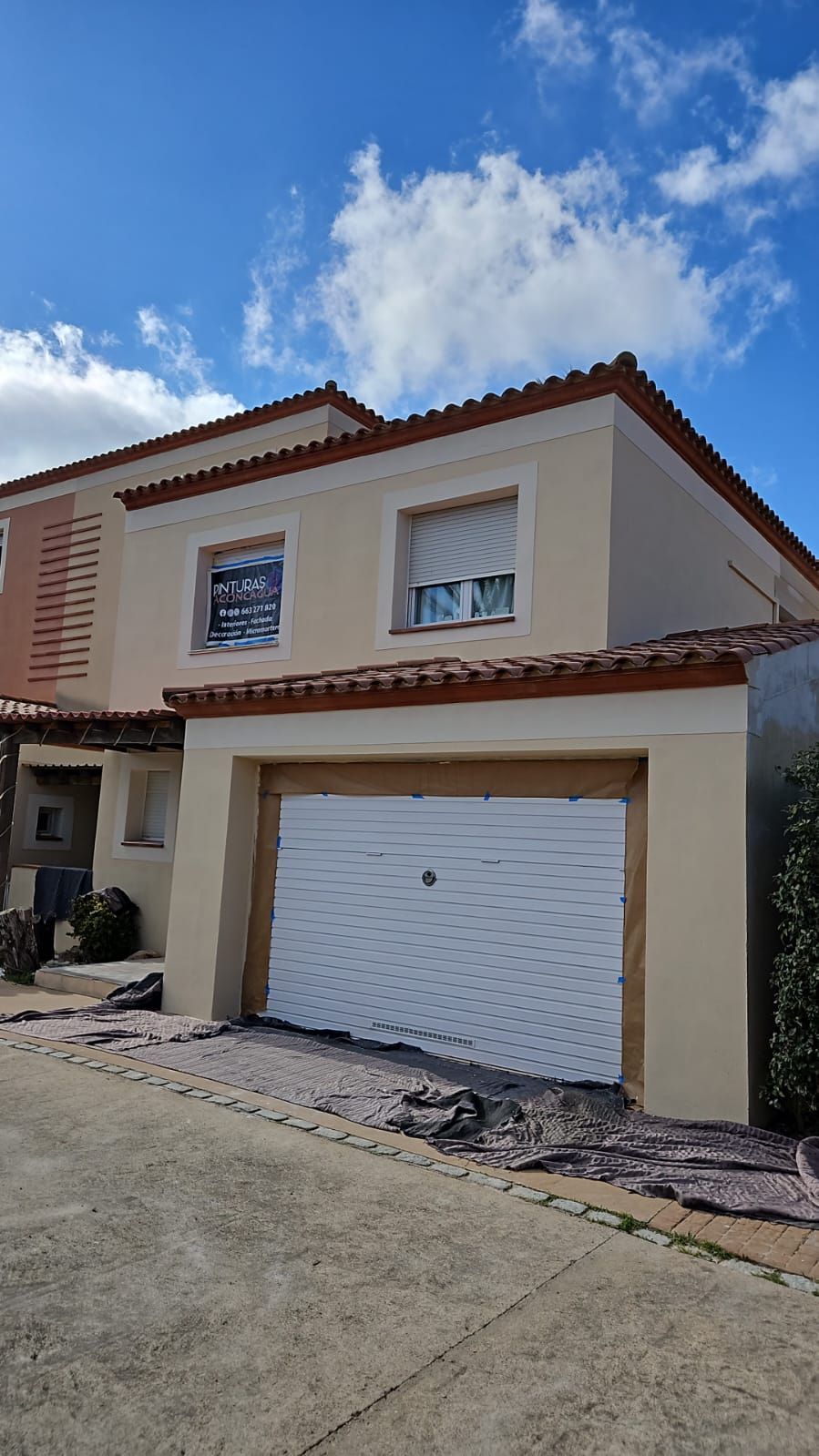 Casa beige de dos pisos con una puerta de garaje blanca bajo un cielo azul brillante