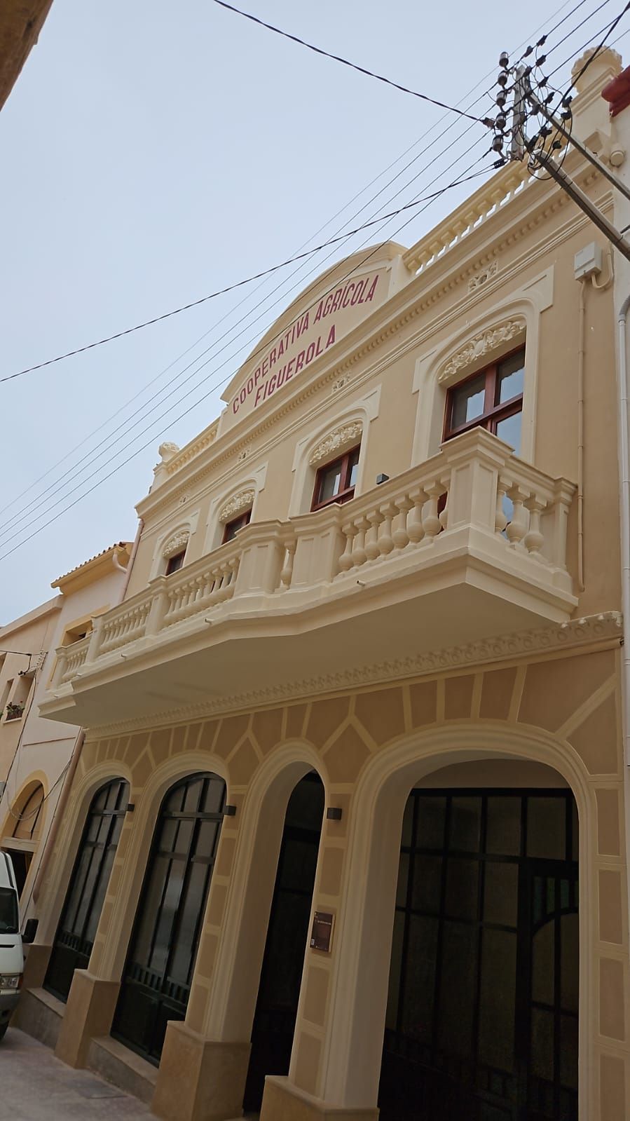 Fachada ornamentada de un edificio histórico de color crema, con puertas arqueadas y balcones bajo un cielo pálido