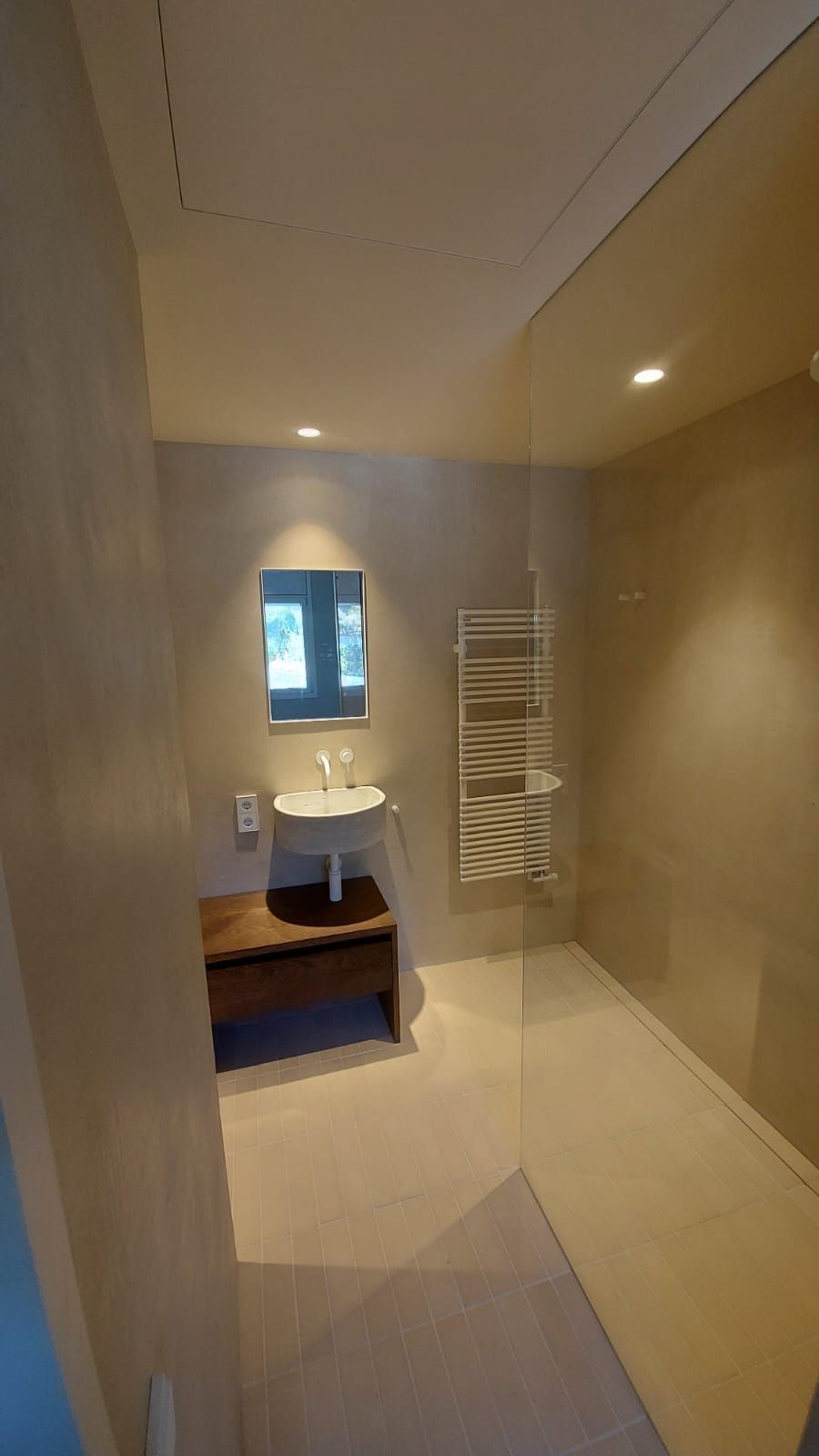 Baño moderno pequeño con azulejos beige, zona de ducha, lavabo, espejo y toallero.