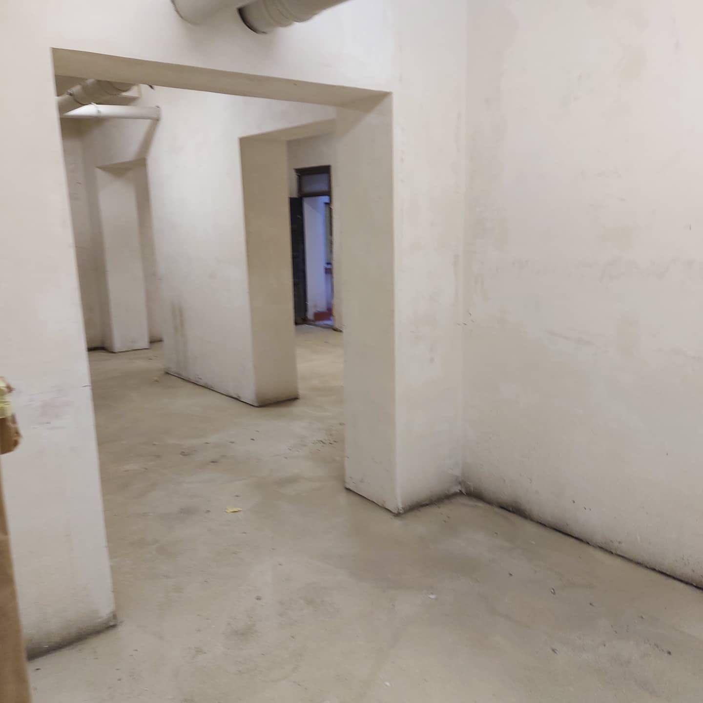 Pasillo estrecho y blanco, con paredes sin terminar, suelo de hormigón y puertas que conducen al interior.