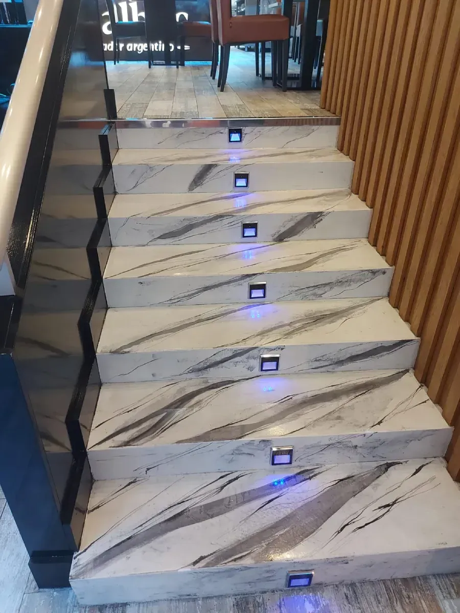 Escalera de mármol con luces azules en los escalones y una barandilla de madera a la derecha