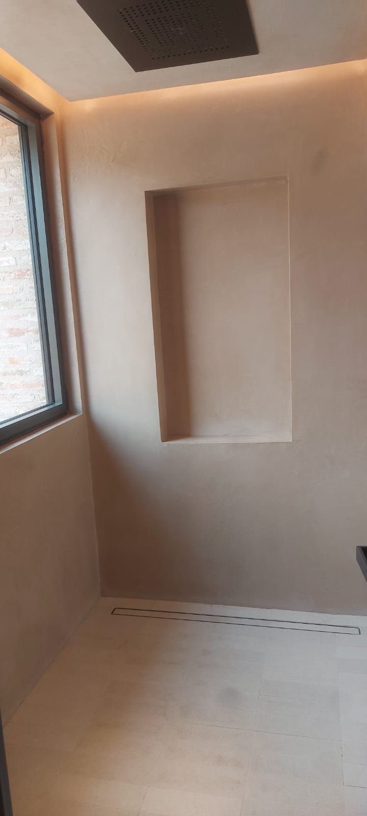Habitación pequeña sin terminar, con paredes beige, una ventana a la izquierda y un nicho empotrado en la pared.