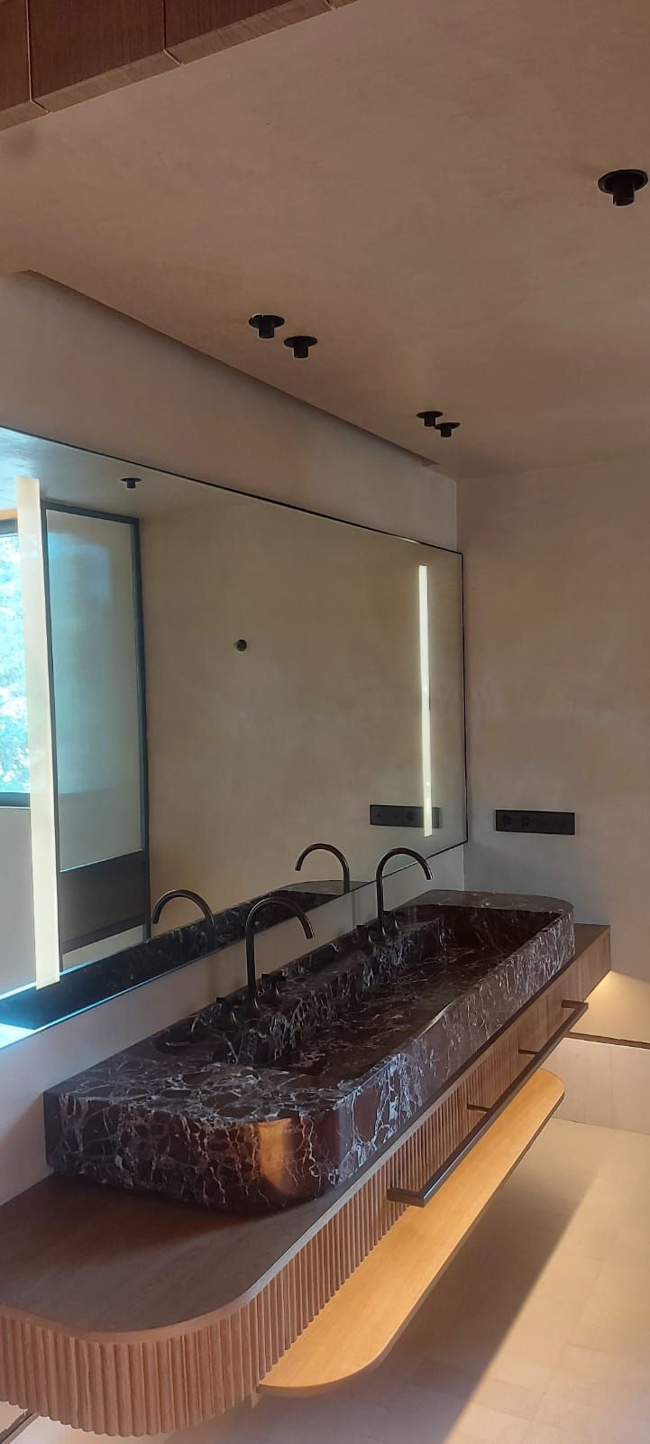 Baño moderno con una larga encimera de mármol con lavabo, espejo y grifos empotrados en la pared bajo una iluminación tenue