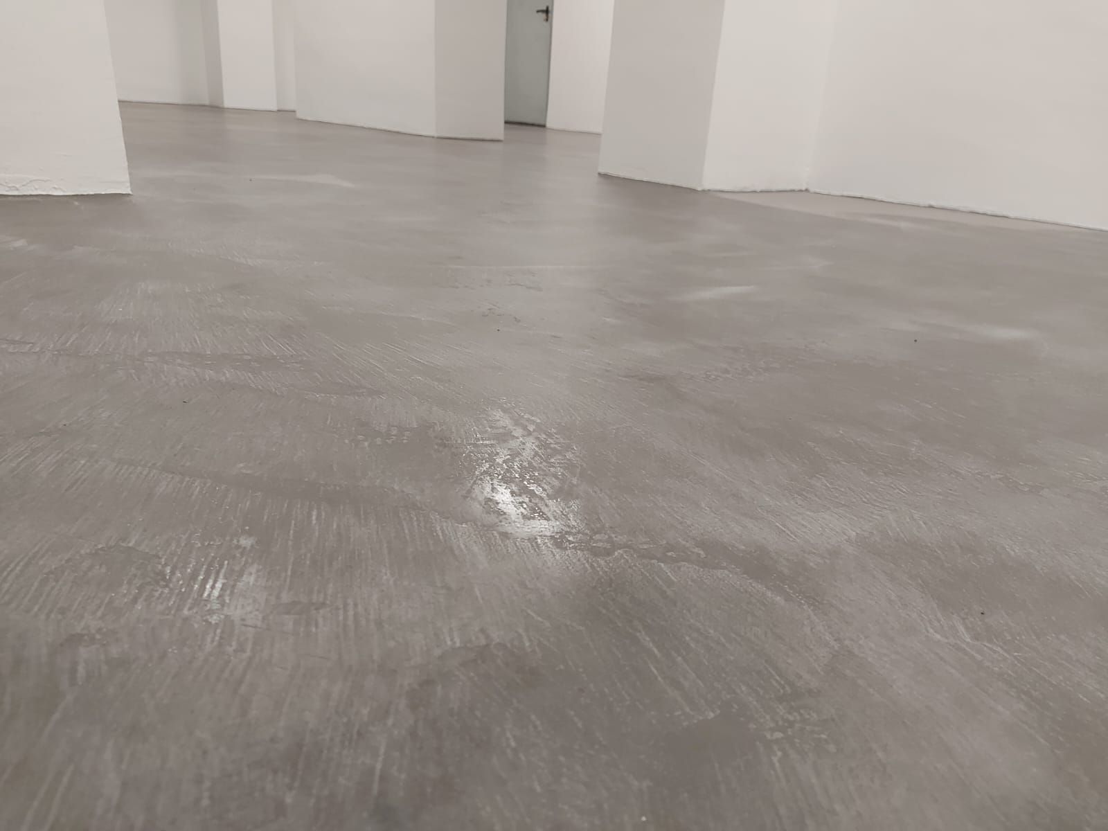 Habitación vacía con suelo gris, paredes blancas y columnas