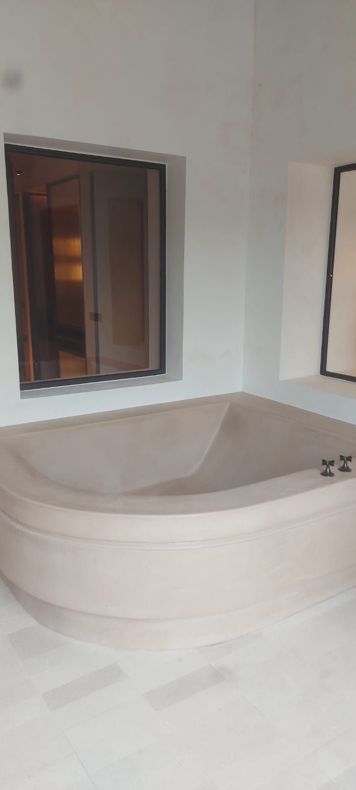 Baño moderno con una amplia bañera esquinera bajo una ventana y un espejo de pared.