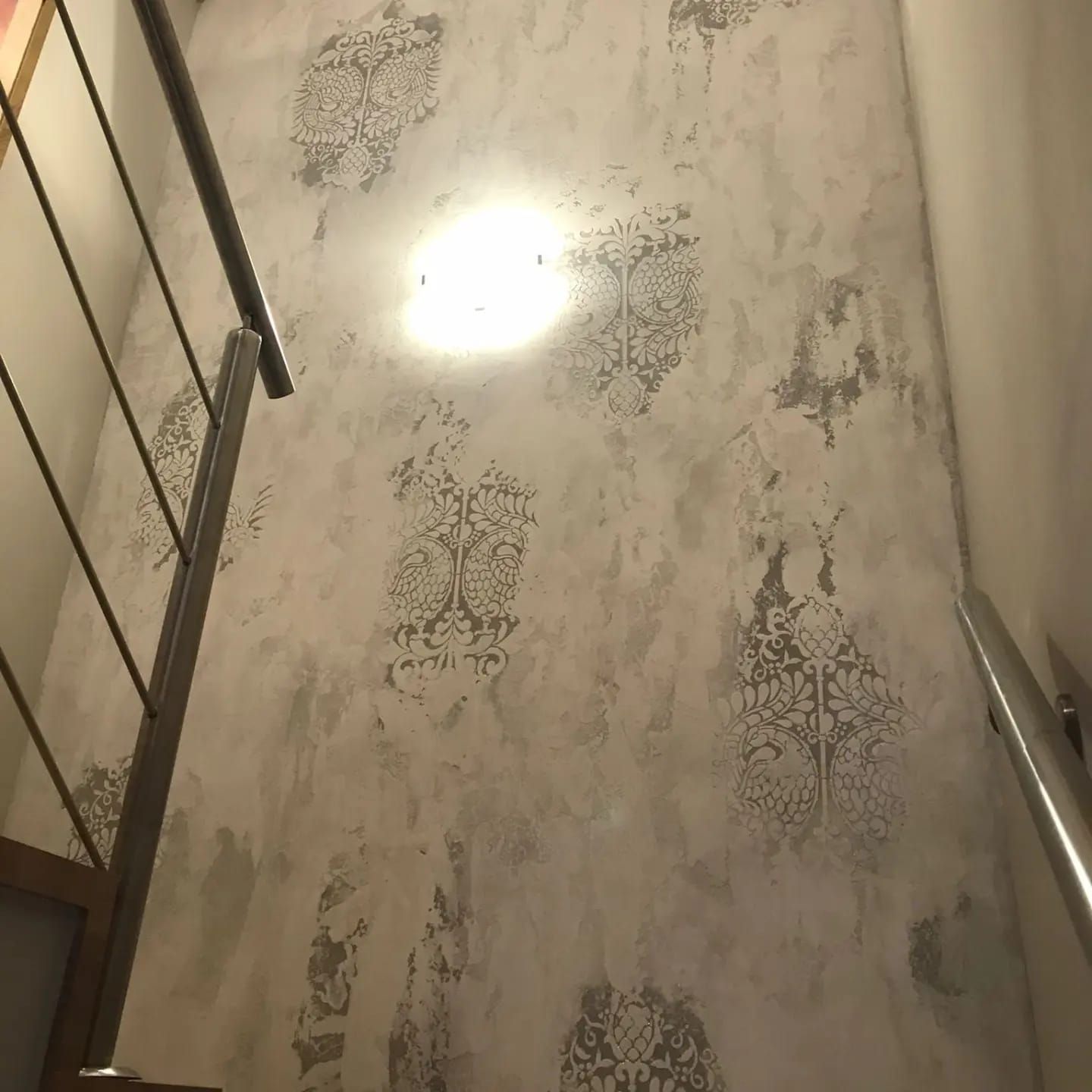 Pared de la escalera con papel pintado estampado y una luz de techo brillante, vista desde abajo