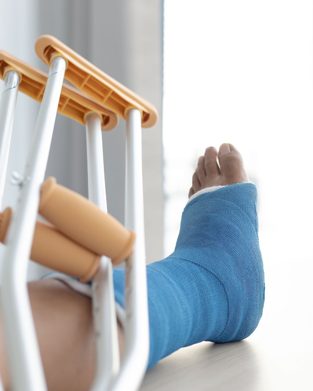 Una pierna con una escayola azul descansa cerca de un par de muletas.