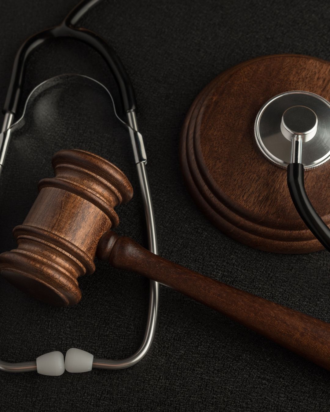 Un mazo de juez de madera y un estetoscopio descansan sobre un fondo oscuro y texturizado.