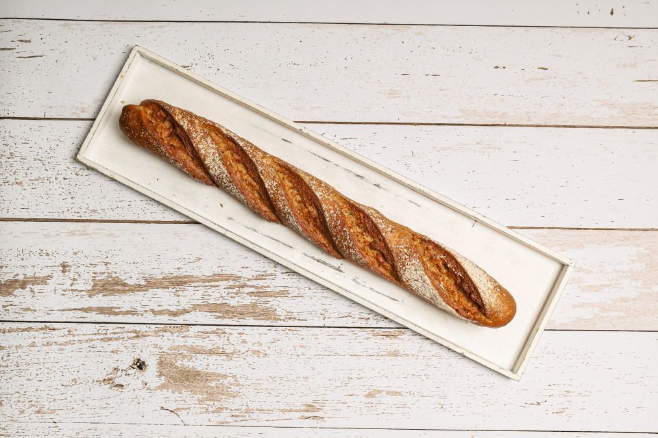 Ein langes Baguette auf einer rechteckigen weißen Platte, die auf einer weißen Holzoberfläche steht.