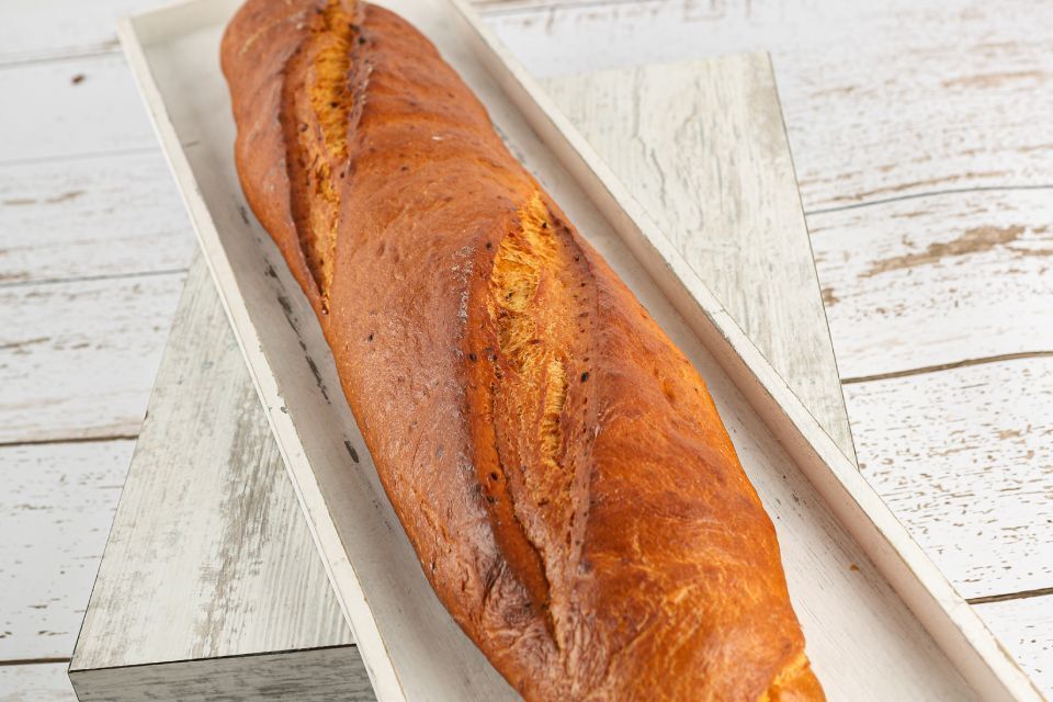 Frisch gebackenes Baguette in einem weißen Holztablett auf einer hellen Holzoberfläche.