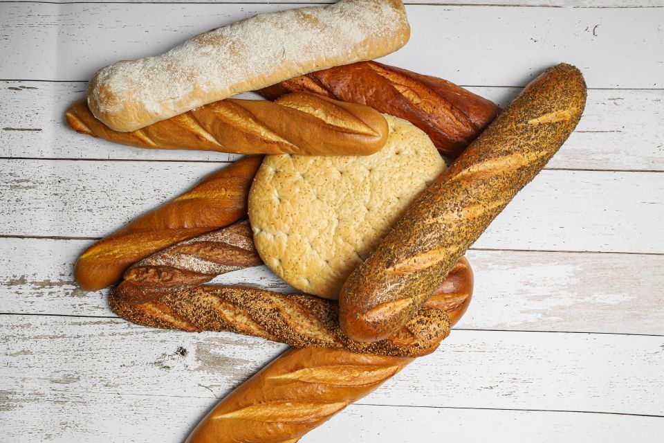 Eine Auswahl verschiedener Brotsorten, darunter Baguettes und Fladenbrot, auf einer weißen Holzoberfläche.