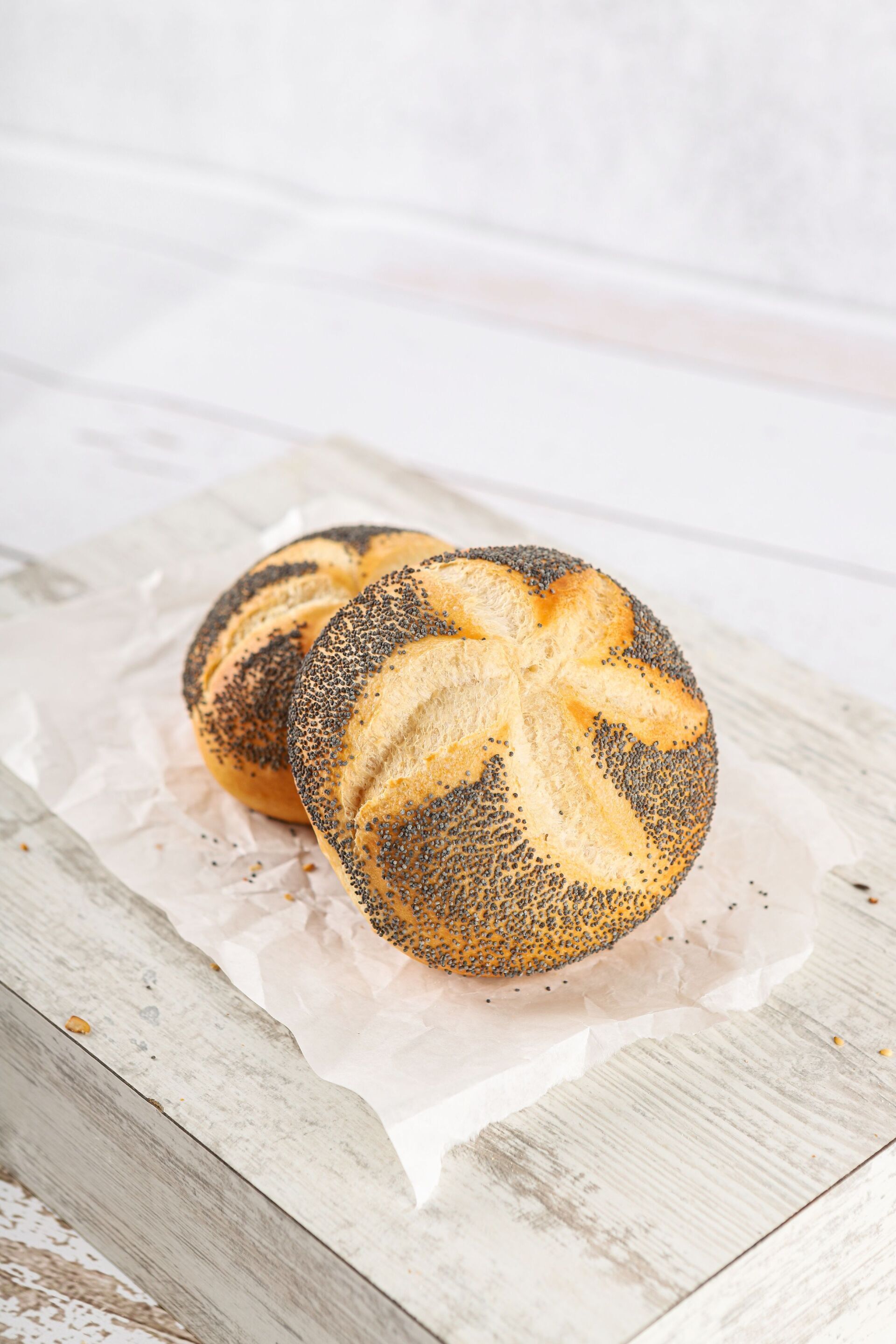 Zwei Mohnbrötchen auf weißem Pergamentpapier.
