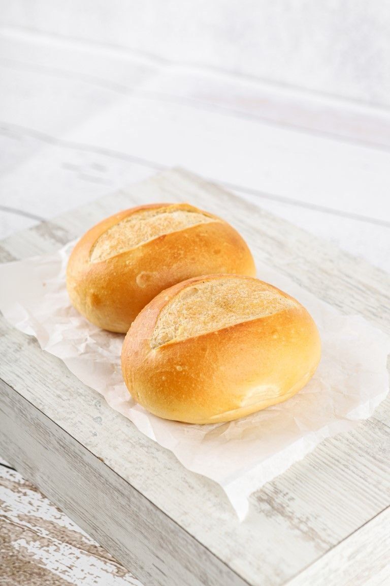 Zwei goldbraune Brötchen liegen auf weißem Pergamentpapier auf einer hellen Holzoberfläche.