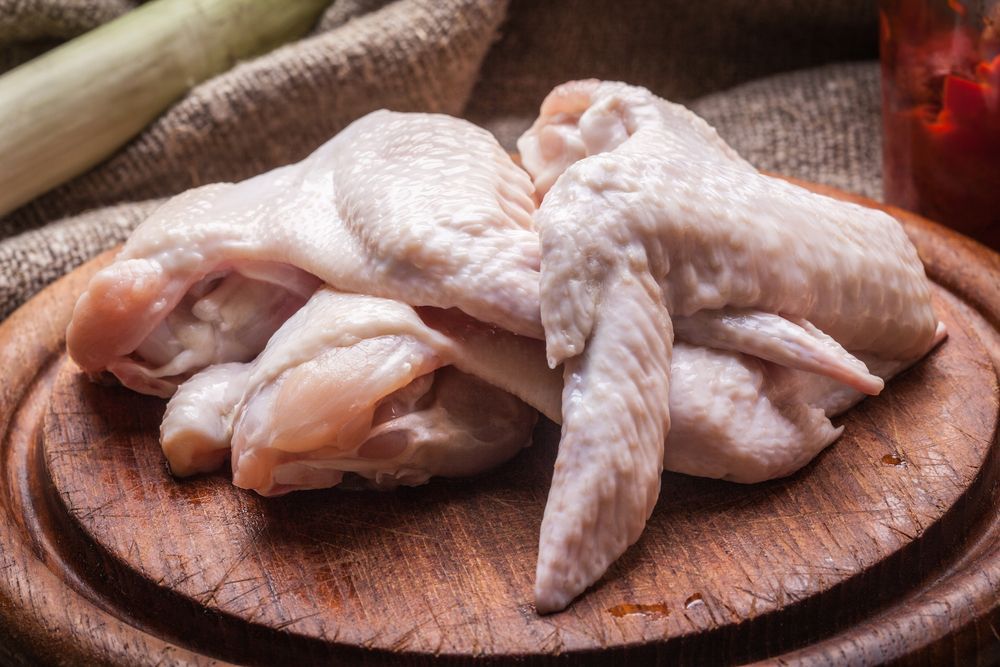 Alitas de pollo crudas sobre una tabla de cortar de madera.