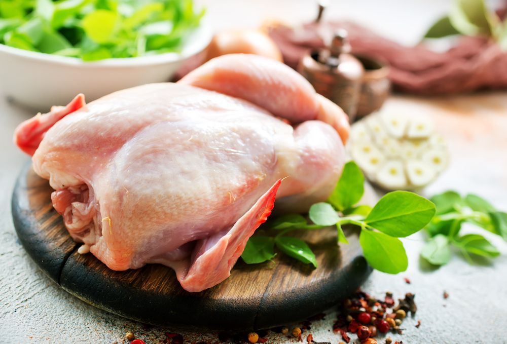 Un pollo crudo está sentado sobre una tabla de cortar de madera.