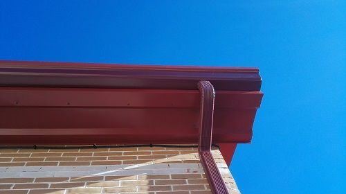 Una canaleta roja en un edificio de ladrillo con un cielo azul de fondo.
