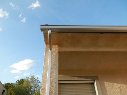 Una casa con una canaleta a un lado y un cielo azul al fondo.