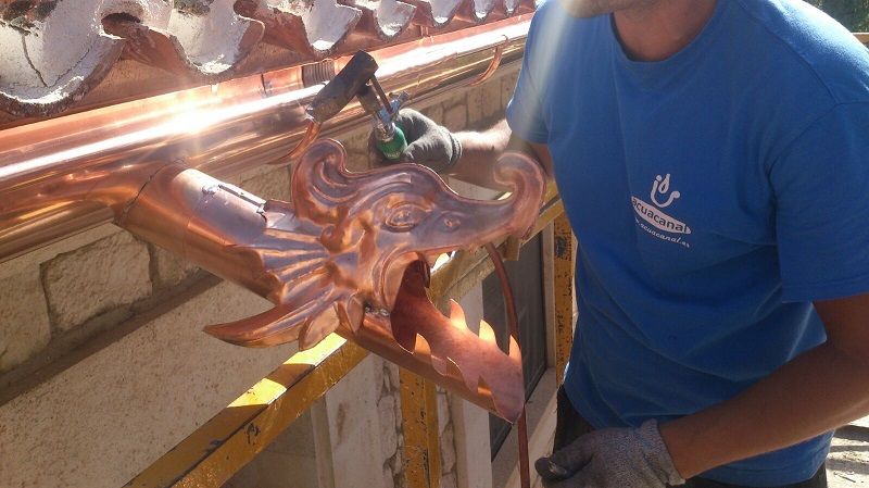 Un hombre con camisa azul está trabajando en una canaleta de cobre.