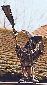 Una estatua de una bruja sosteniendo una escoba en lo alto de un tejado.