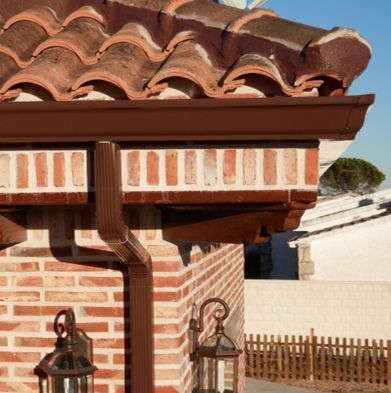 Un edificio de ladrillo con un canalón marrón y un techo de tejas.