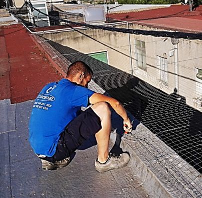 Un hombre con una camisa azul está arrodillado en un tejado.