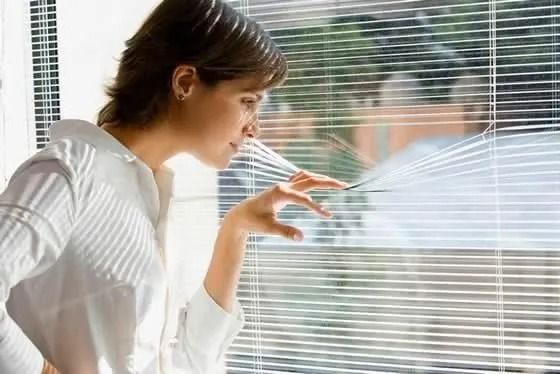 Una mujer mira por una ventana con persianas.