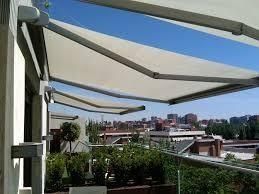 Toldos retráctiles sobre un balcón, que proporcionan sombra en un día soleado con vistas a la ciudad.
