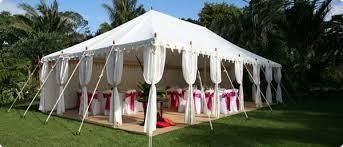 Carpa blanca instalada sobre césped verde, con tela blanca drapeada y mesas en su interior.