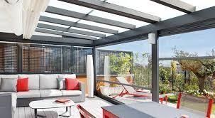 Moderno espacio exterior con sofá gris, mesa blanca, sillas rojas y paredes de cristal.