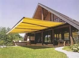 Toldo amarillo sobre el patio de madera de una casa, en un día soleado.