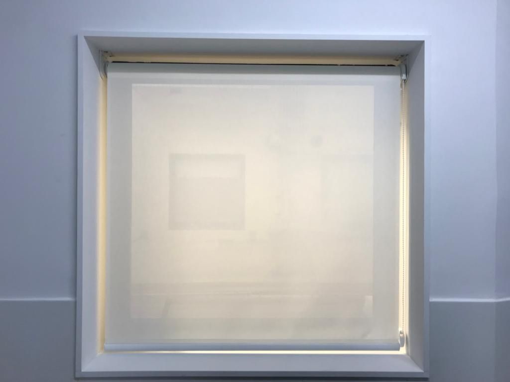 Una persiana blanca está colgada en una ventana de una habitación.