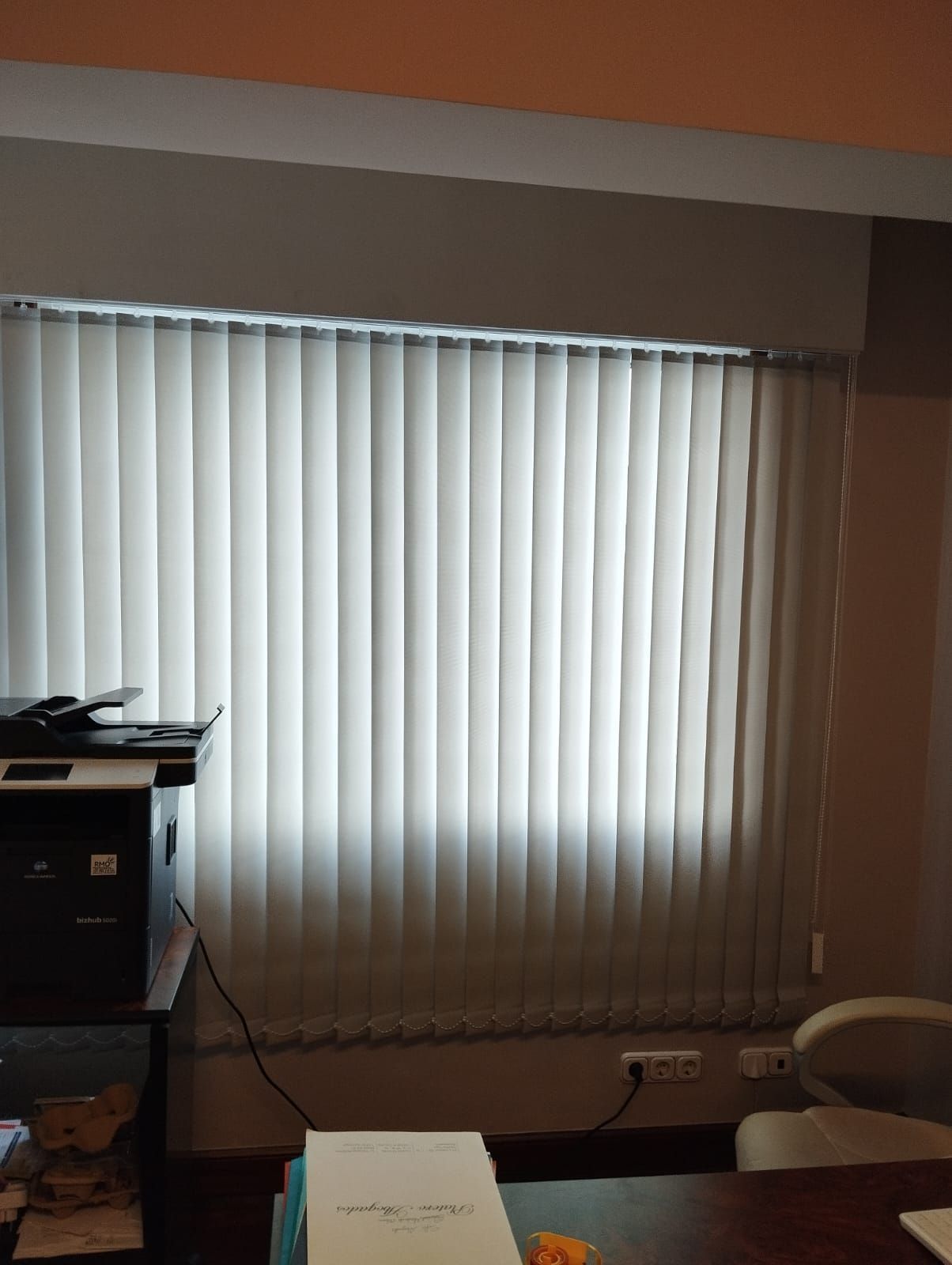 Una habitación con persianas verticales blancas y un escritorio.