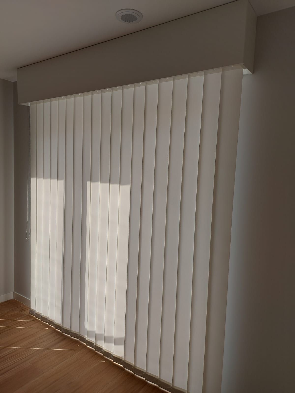 Una habitación con persianas verticales en una ventana grande.