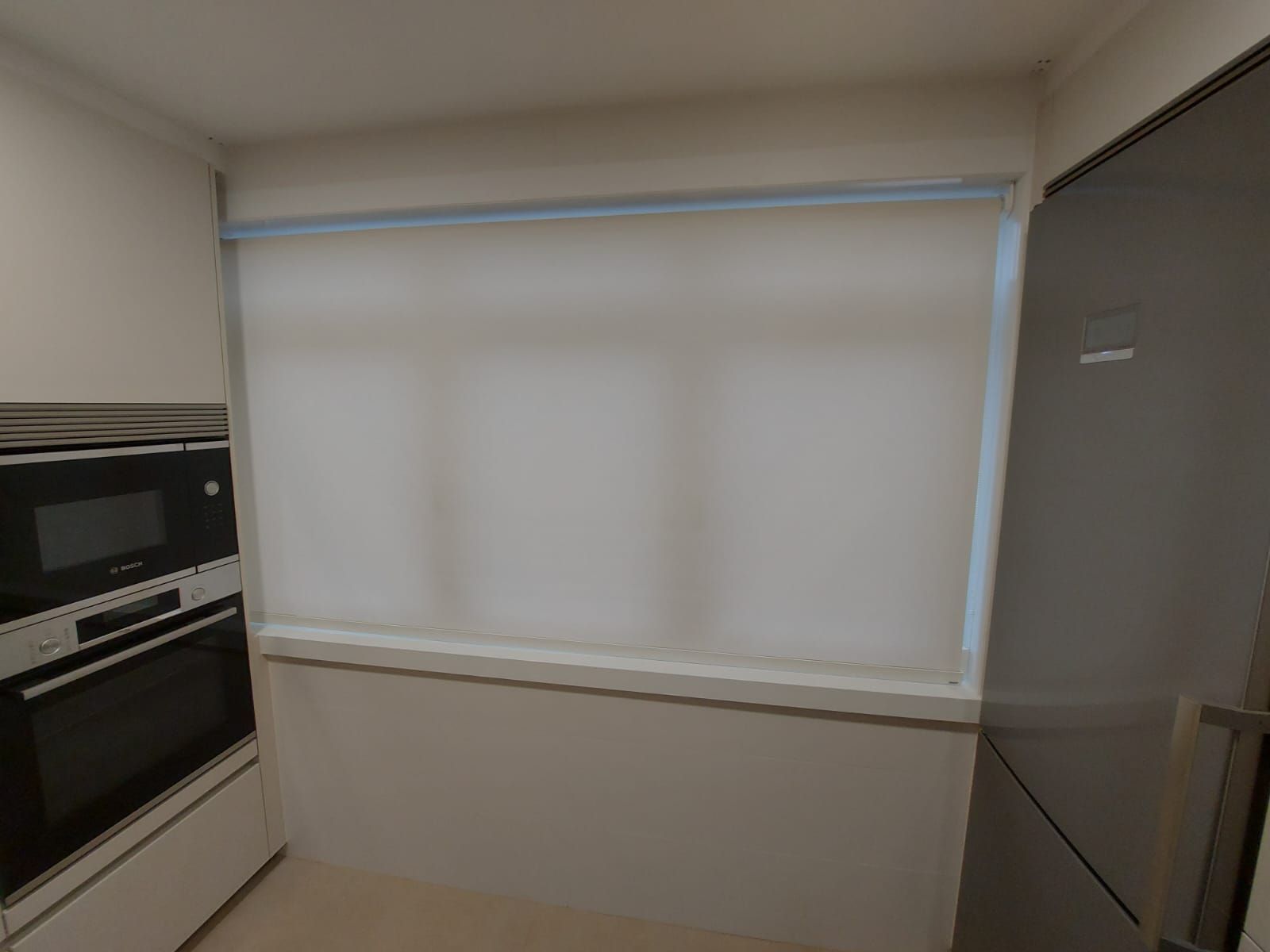 Una cocina con frigorífico, horno, microondas y persianas en la ventana.