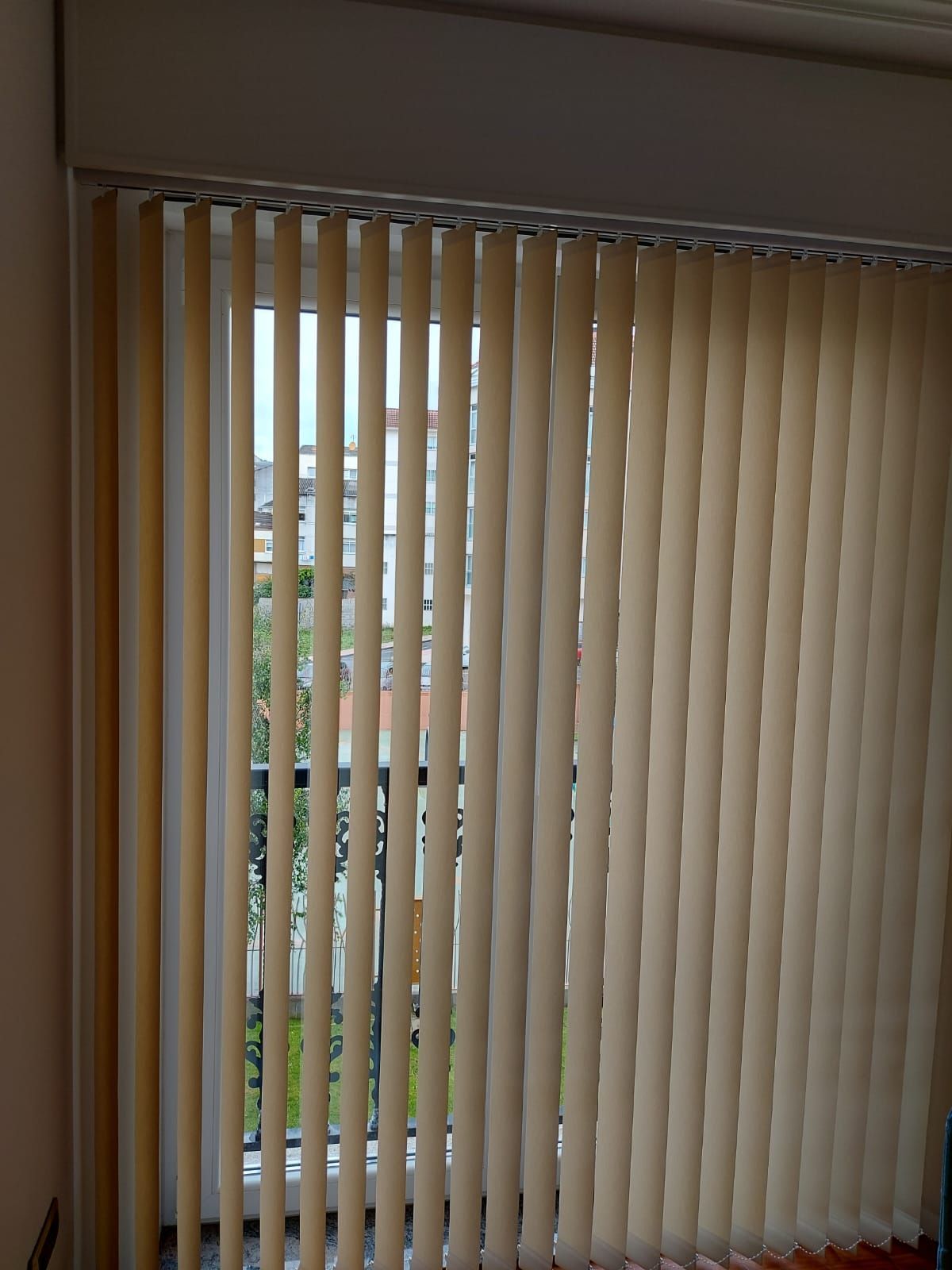 Una ventana con persianas verticales y un balcón al fondo.