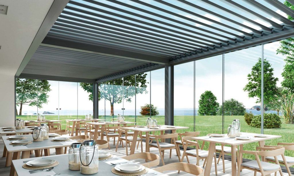 Un restaurante con mesas y sillas bajo una pérgola con vista al mar.