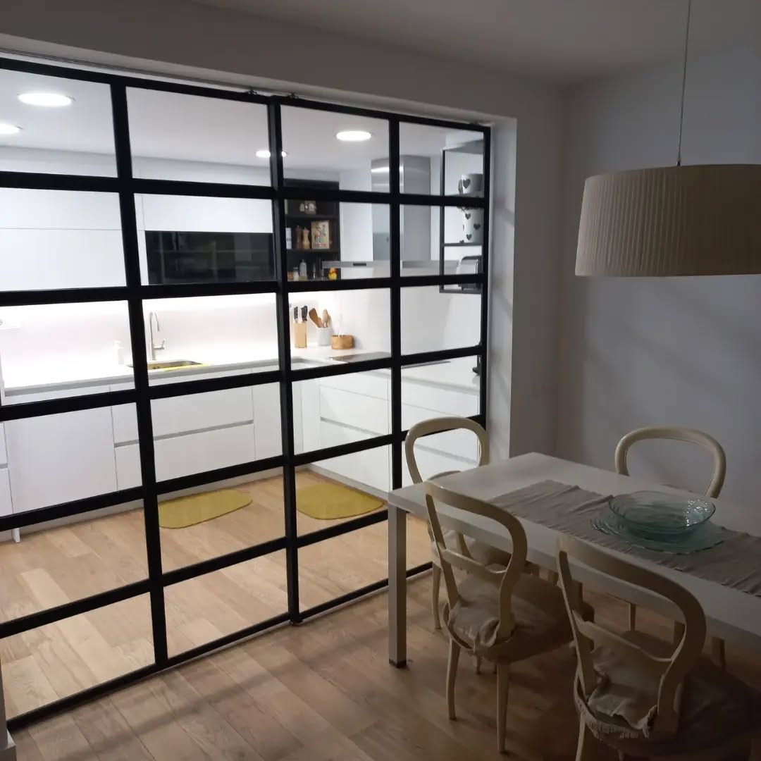 Un comedor con una mesa y sillas detrás de una pared de vidrio.